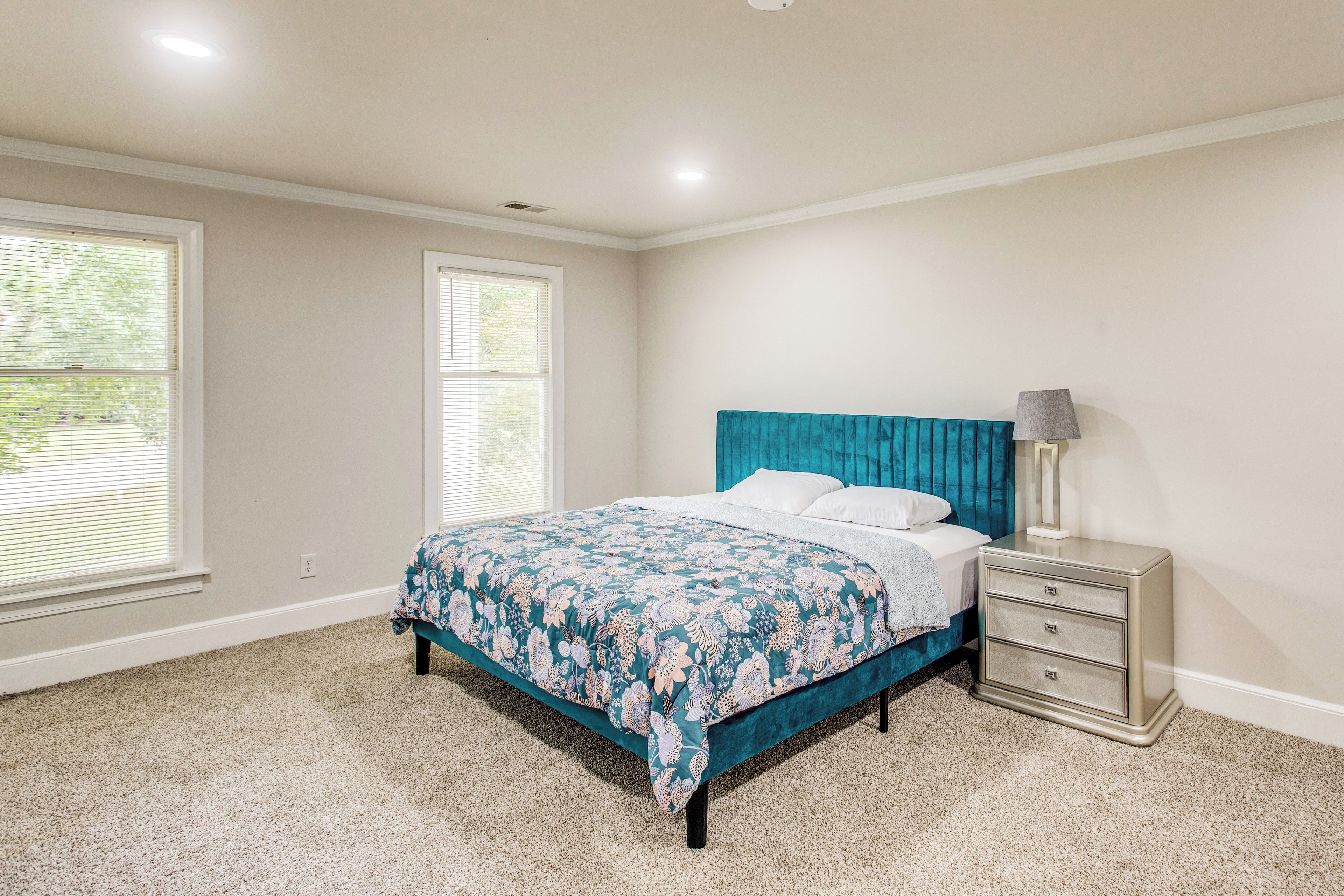 A bedroom with a bed, a nightstand, and two windows.