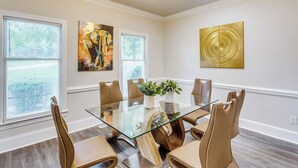 A modern dining room with a glass table surrounded by six chairs, two potted plants, and two artworks on the walls. - 3-story Home w/ Private Backyard in Florence! (Florence)