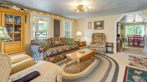 A cozy living room with a floral sofa, a wooden coffee table, and a bookshelf. - 2 Mi to Hiking Trails: Cozy Fayetteville Cottage! (Fayetteville)
