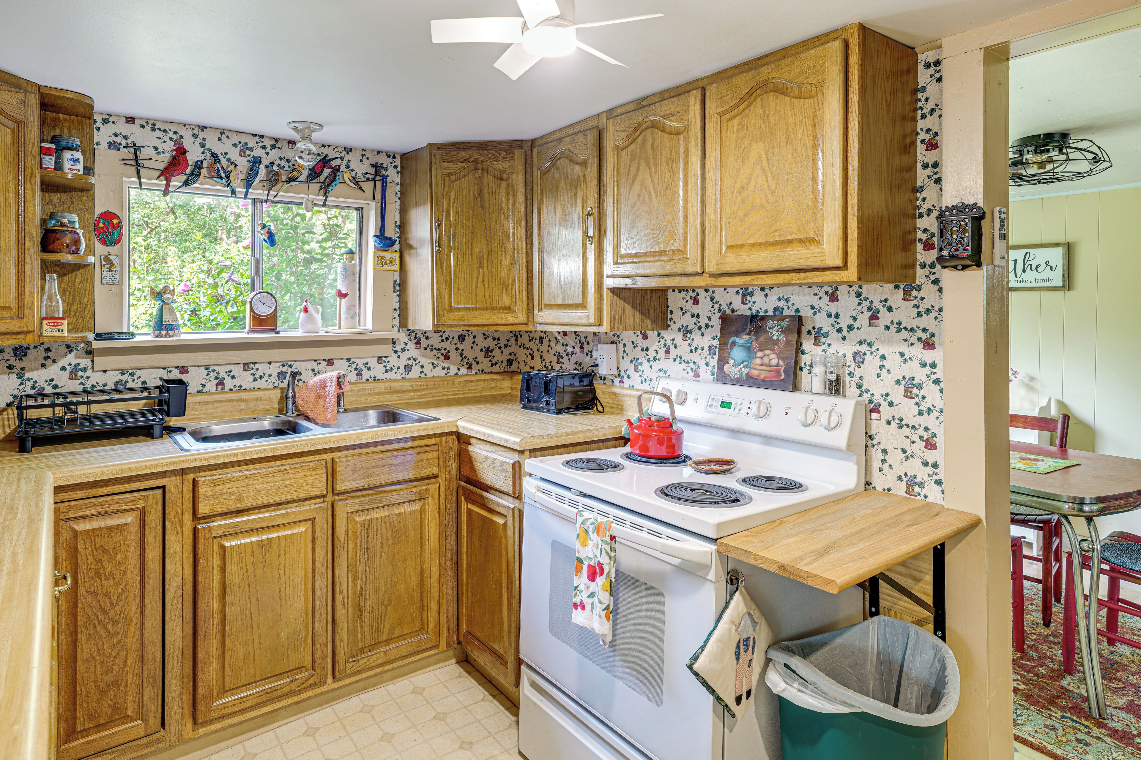 A kitchen with wooden cabinets, a stove, and a window with a view of greenery.