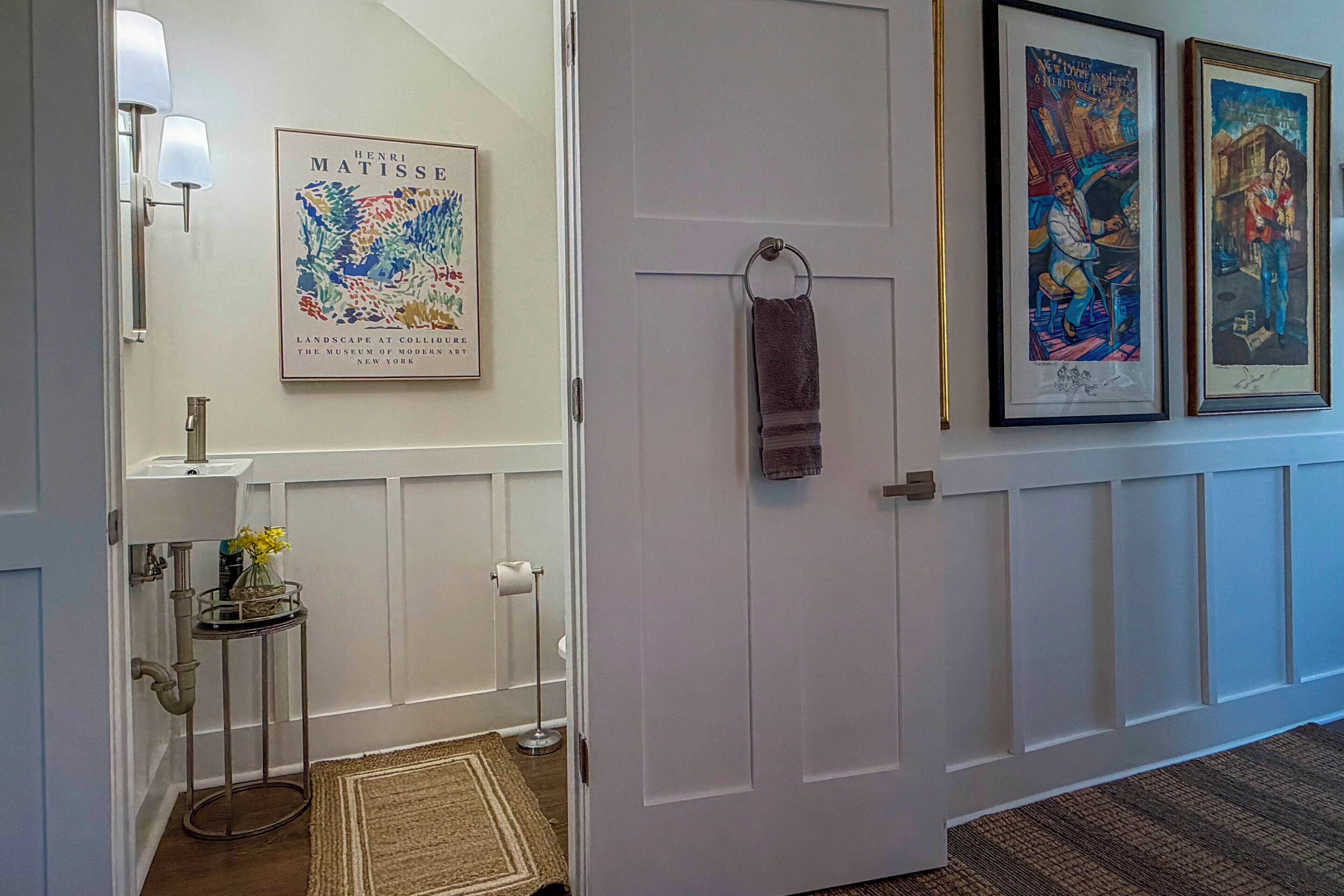Un pasillo con una obra enmarcada de Henri Matisse, una puerta con una toalla colgada y una mesita con un florero.