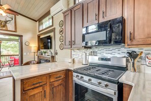 A kitchen with wooden cabinets, a stainless steel stove, and a microwave. - 1 Mi to Tank Town Usa: Tiny Home w/ Pool Access! (Morganton)