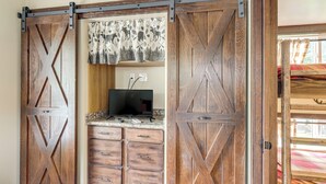 A room with a wooden sliding barn door, a television on a wooden cabinet, and a window with curtains. - 1 Mi to Tank Town Usa: Tiny Home w/ Pool Access! (Morganton)