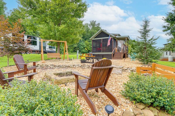 A cabin with a deck, surrounded by a garden with wooden chairs and a swing set. - 1 Mi to Tank Town Usa: Tiny Home w/ Pool Access! (Morganton)