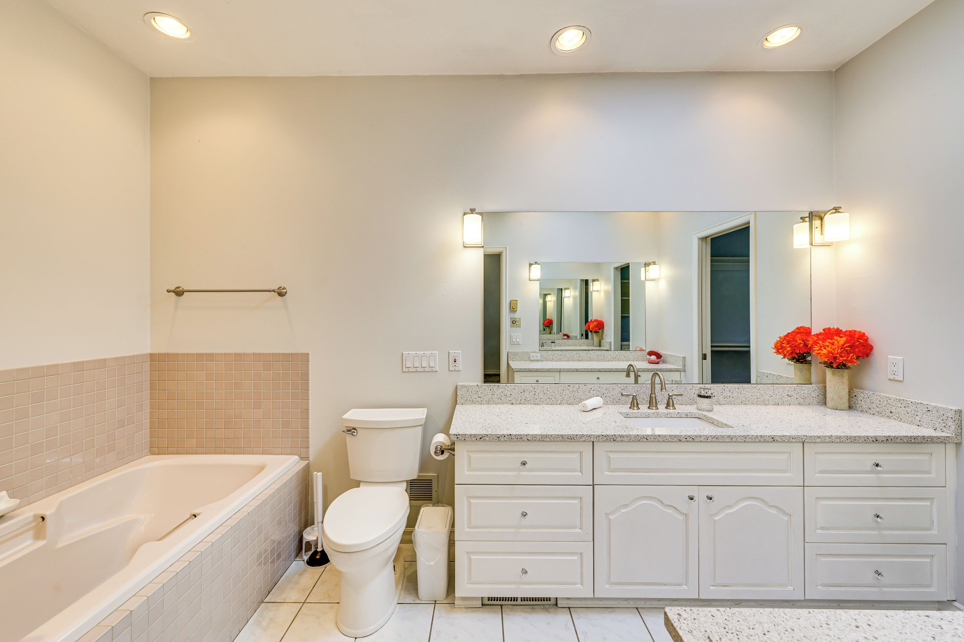 A modern bathroom with a bathtub, toilet, vanity with drawers, and a large mirror.