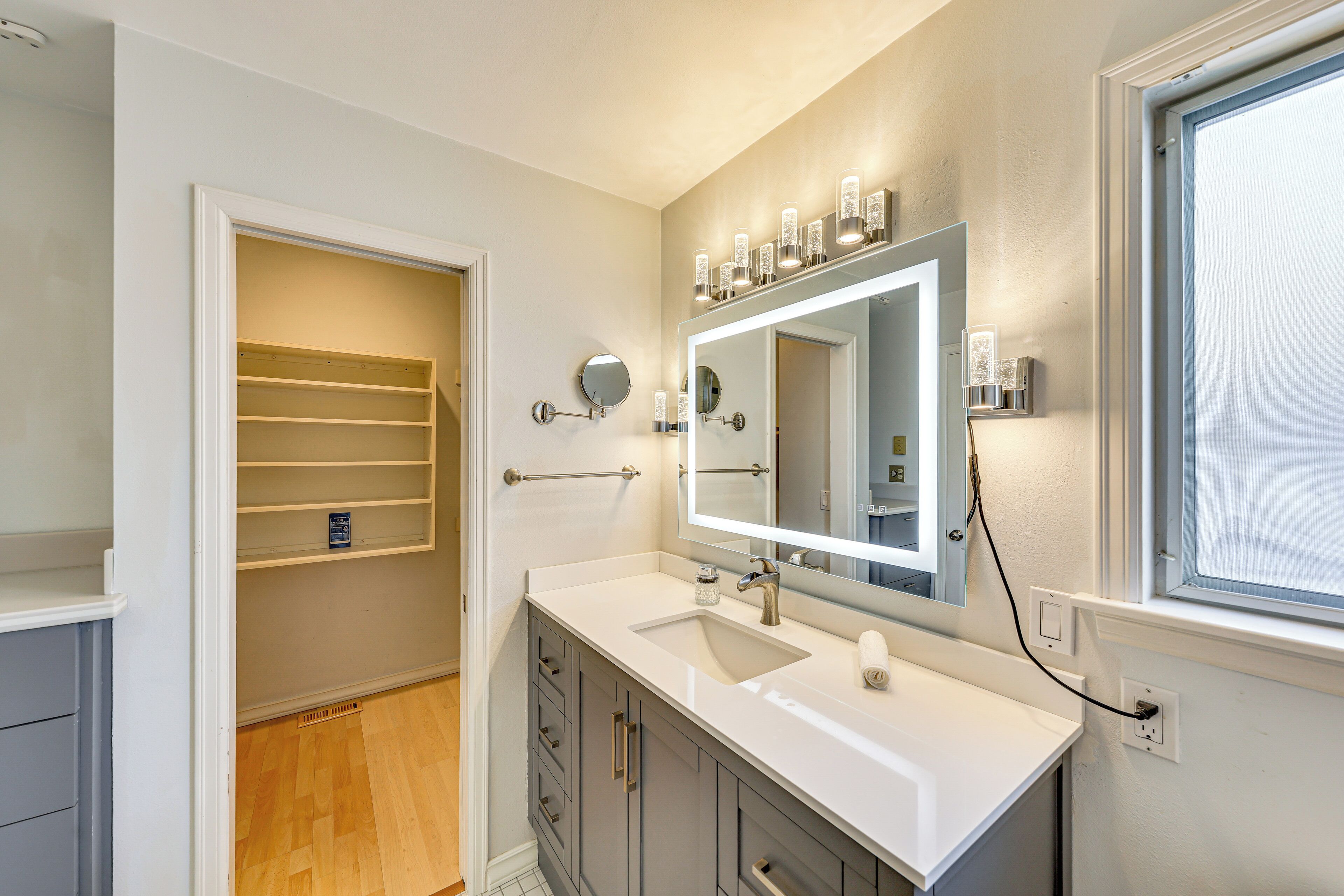 A bathroom with a vanity, a large mirror, a window, and a walk-in closet.
