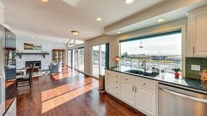 A modern kitchen with a large window, a dining area, and a fireplace. - Waterfront Home w/ Dock, Hot Tub, Fire Pit (Oak Harbor)