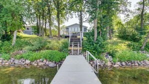 Une jetée en bois menant à une maison entourée d’arbres et bordée d’un petit étang.