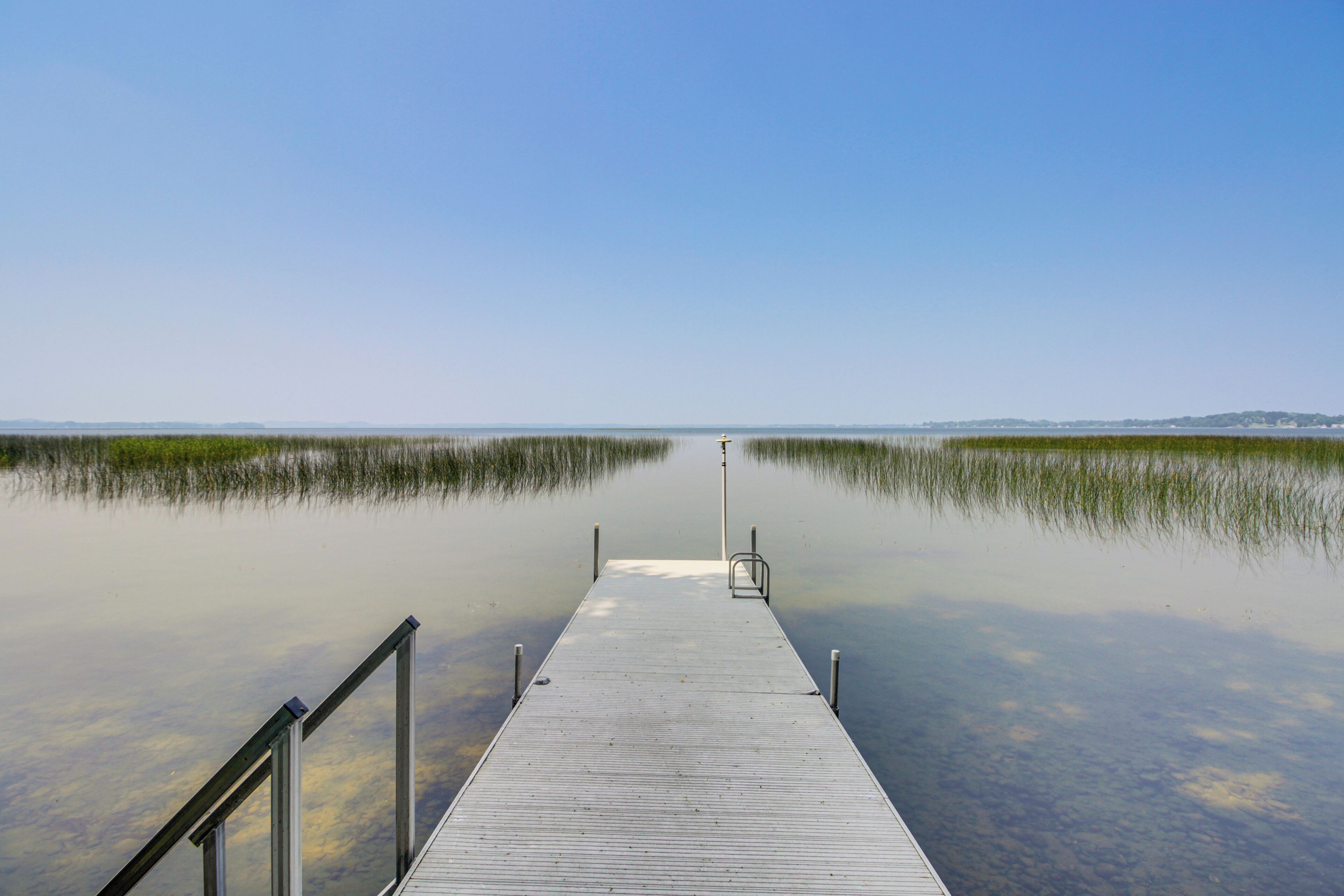 A wooden pier extending into calm water with a metal railing on one side.