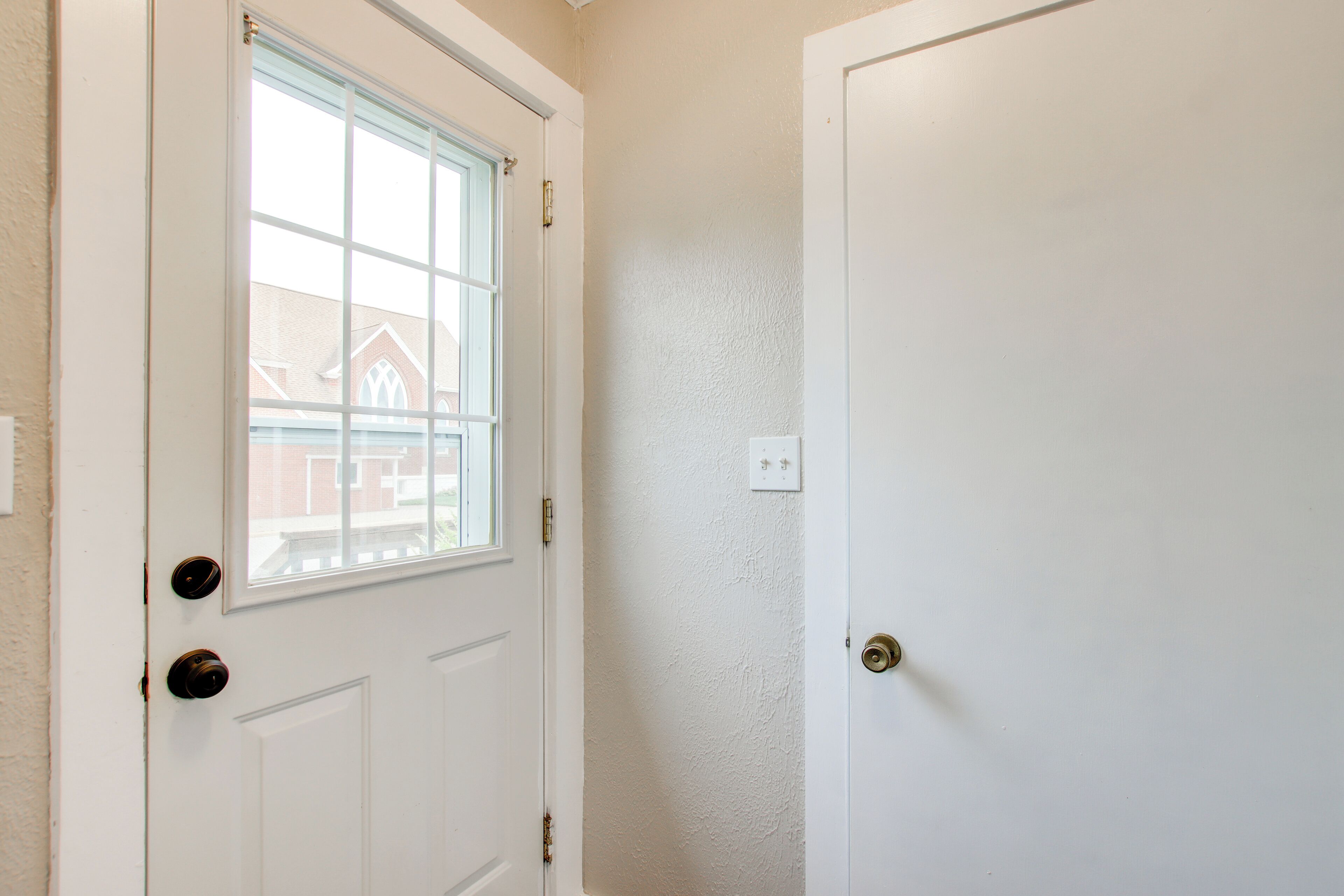 A white door with a window, a doorbell, and a light switch on the wall.
