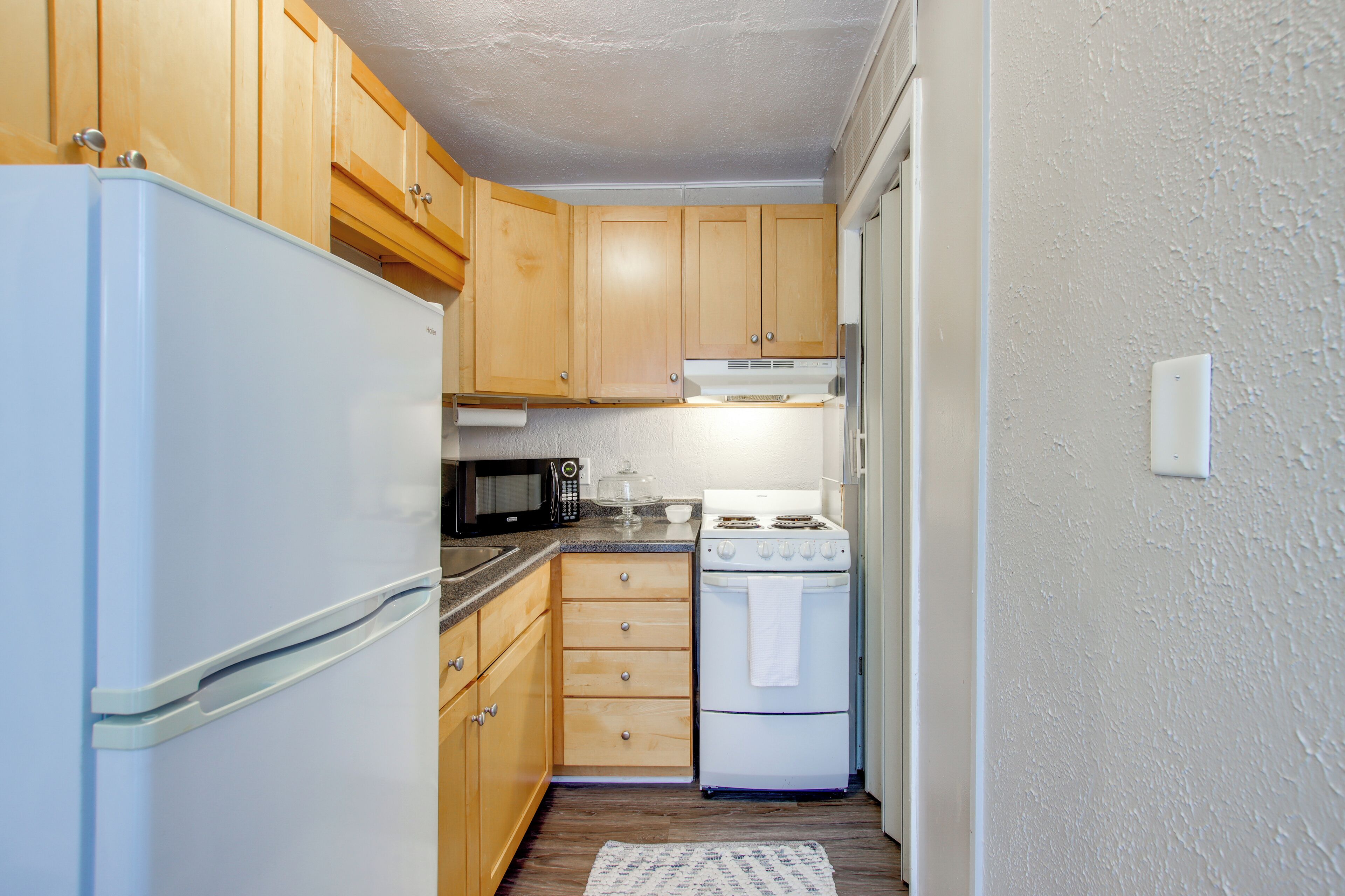 A compact kitchen with wooden cabinets, a white refrigerator, a microwave, a stove, and a sink.