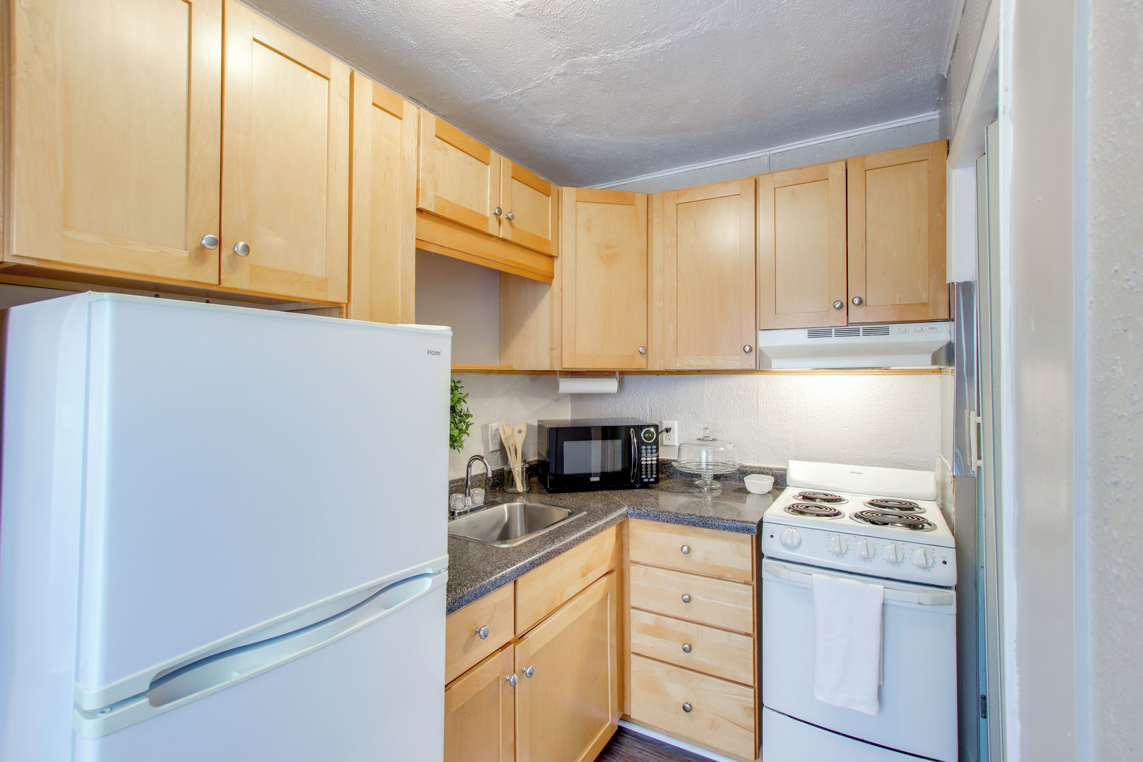 A compact kitchen with wooden cabinets, a white refrigerator, a microwave, a sink, and a stove.
