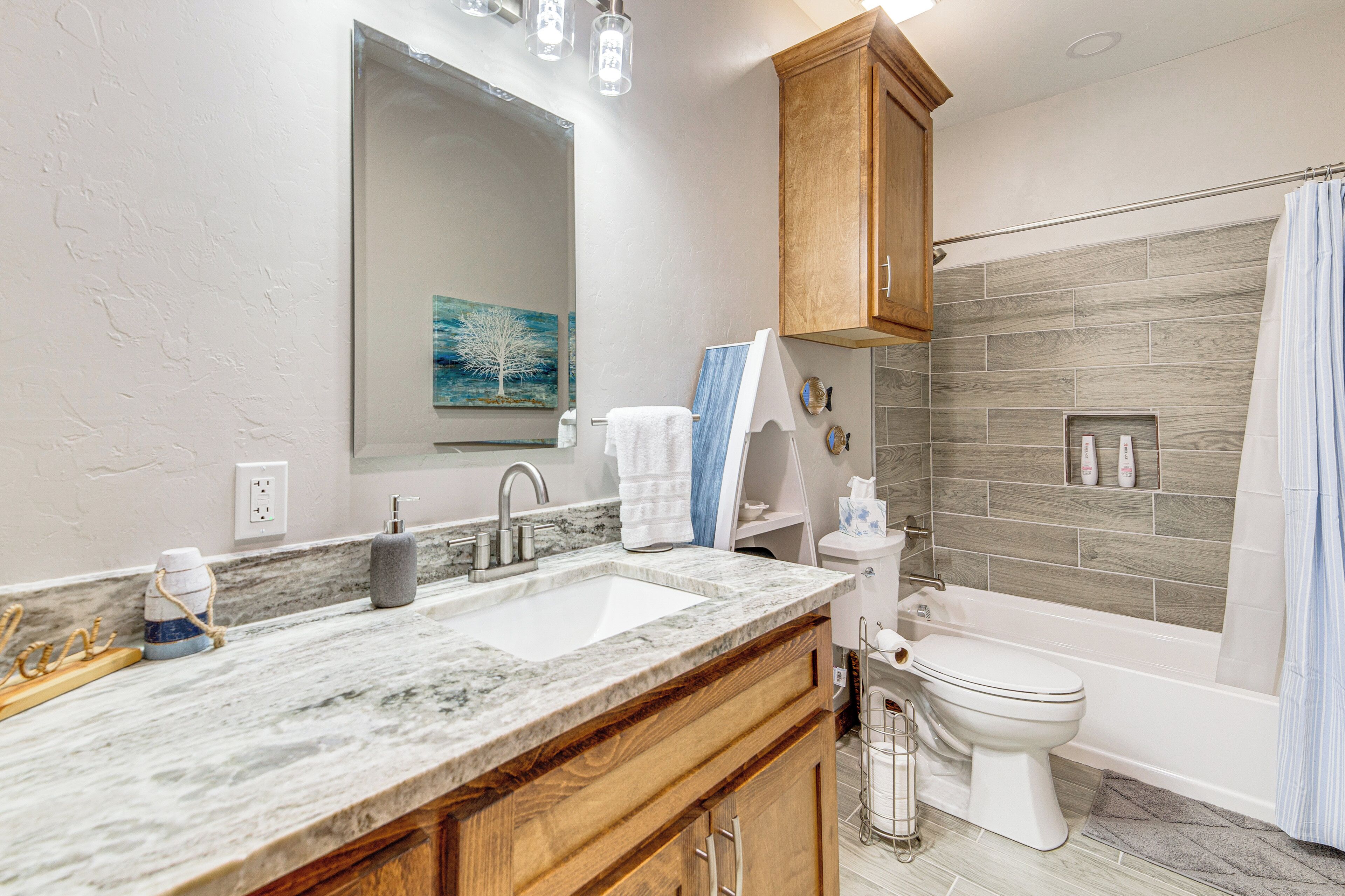 A bathroom with a marble sink, wooden cabinets, a large mirror, a painting, and a shower area.