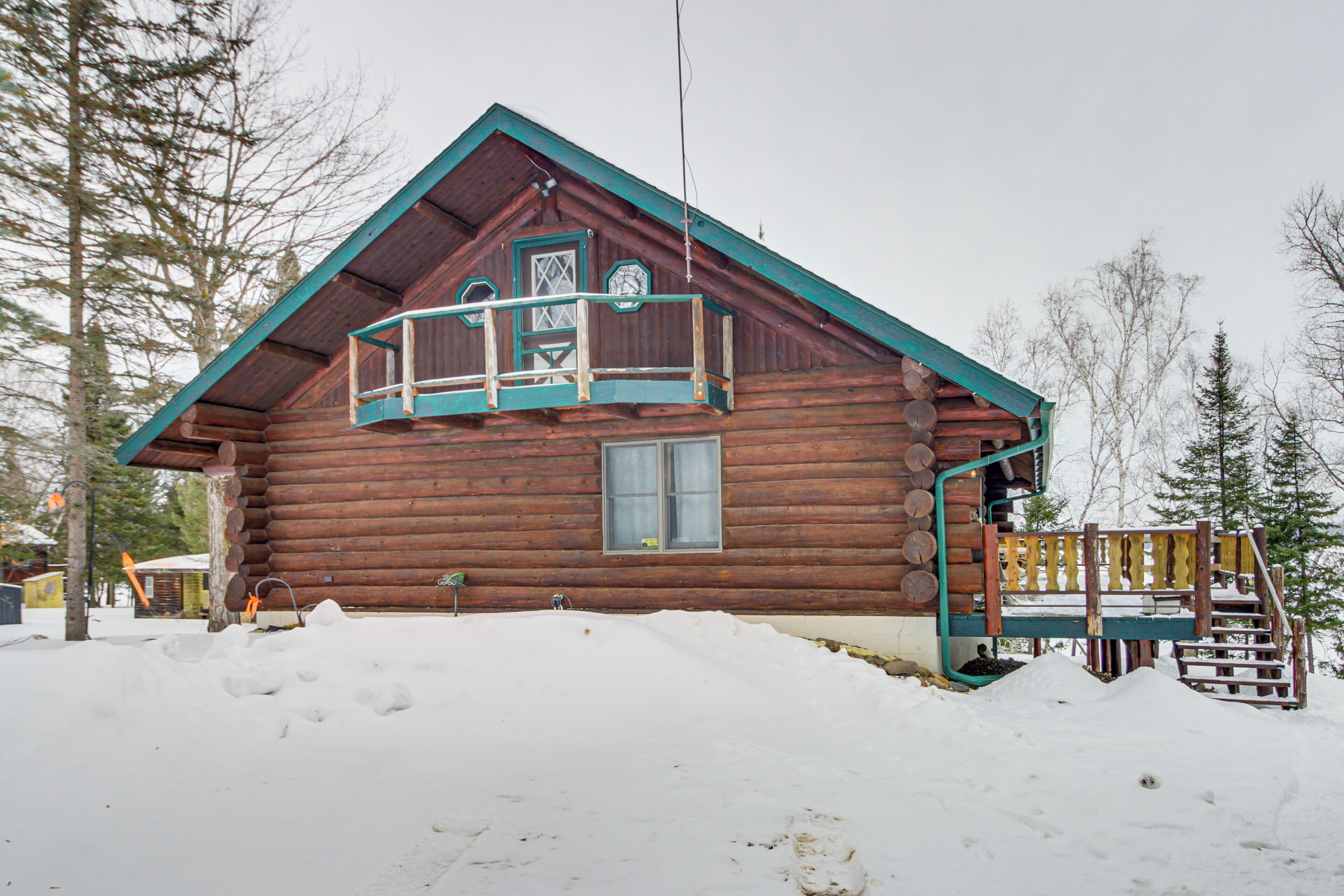 A log cabin with a balcony, surrounded by snow and trees.