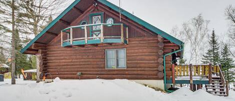 A log cabin with a balcony, surrounded by snow and trees.