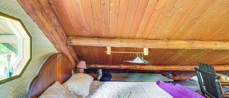 A wooden cabin bedroom with a bed, pillows, a blanket, a wooden chair, and a window.