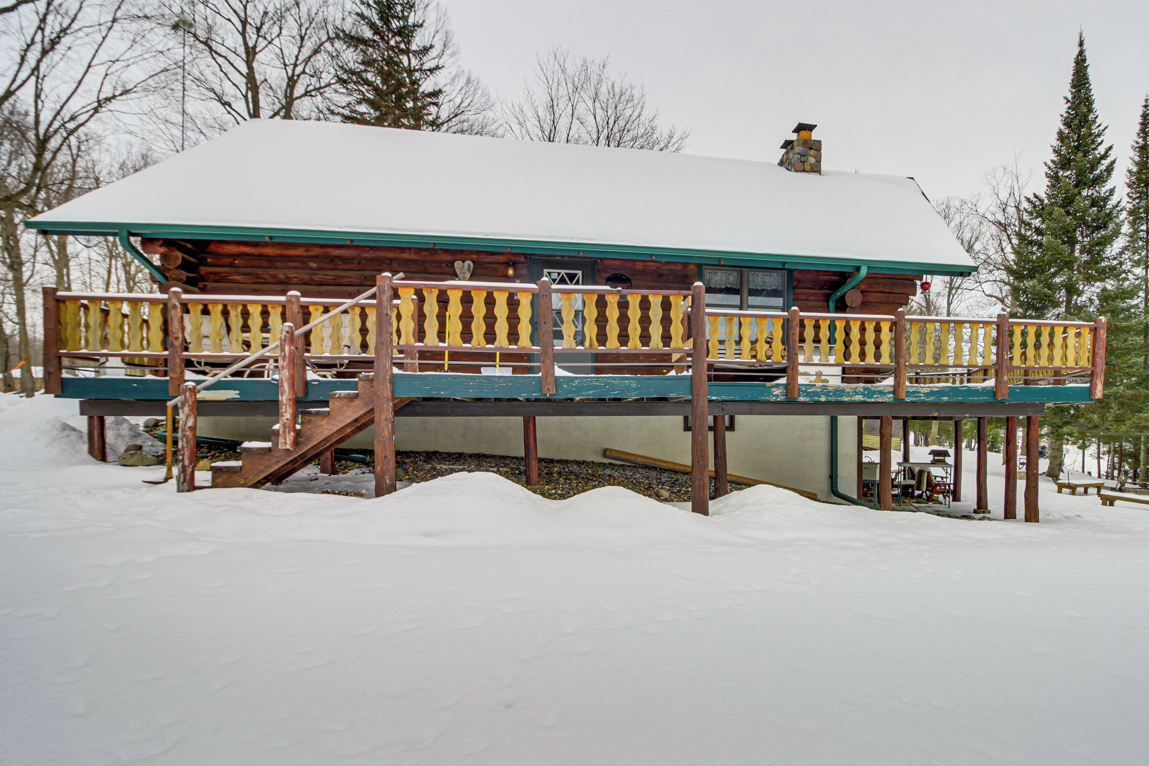 Une cabane en rondins dotée d’une terrasse en bois et d’un escalier menant à une zone abritée.