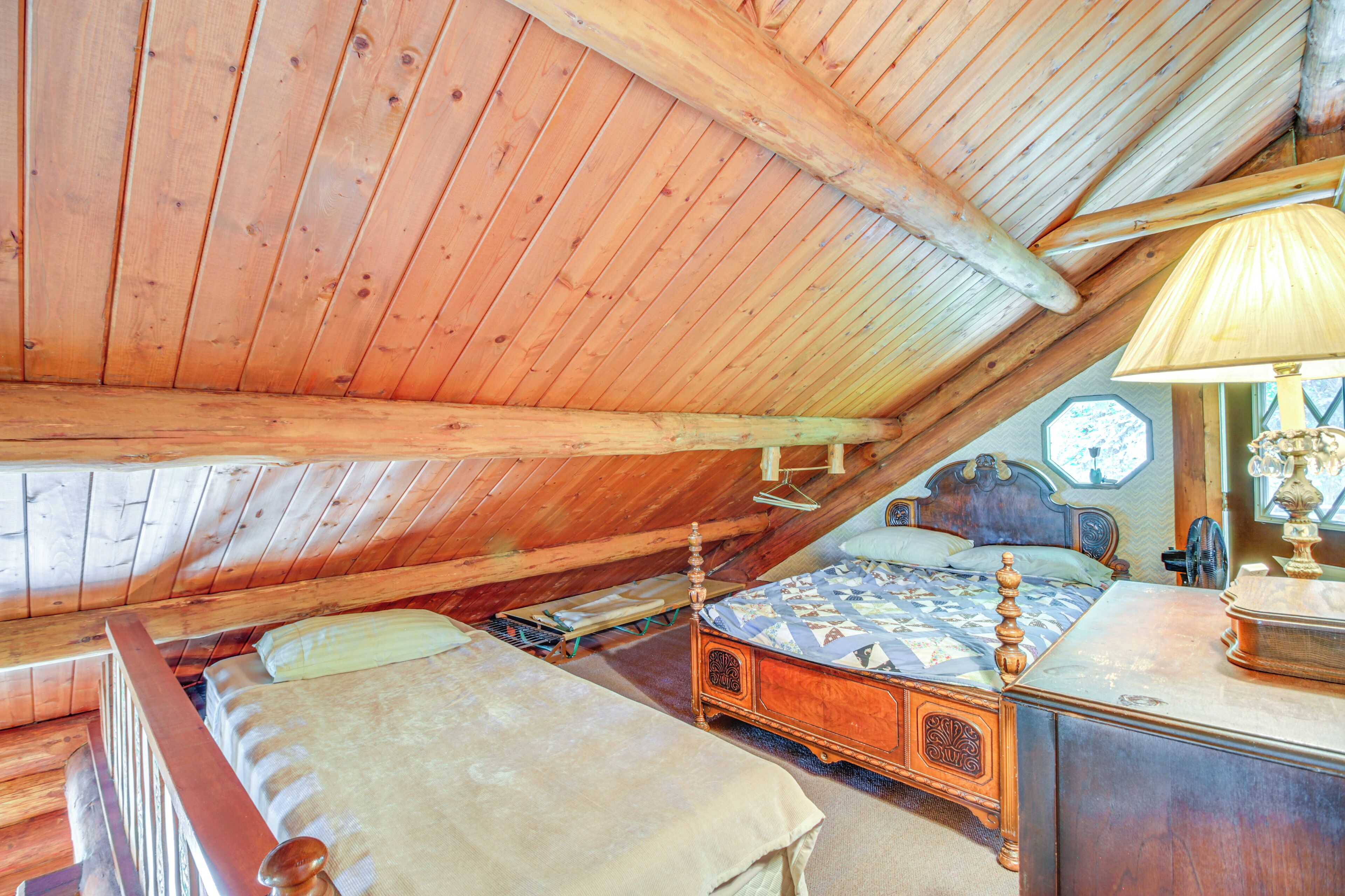 Een houten slaapkamer op zolder met een schuine kap, een bed, een dressoir en een lamp.
