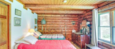 A log cabin bedroom with a bed, dresser, and window.
