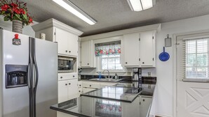 A modern kitchen with white cabinets, a stainless steel refrigerator, a coffee maker, and a window with a floral curtain. - 5 Mi to Downtown Morgan City: Waterfront Retreat (Morgan City)
