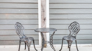 Two metal chairs and a small round table against a wooden wall.