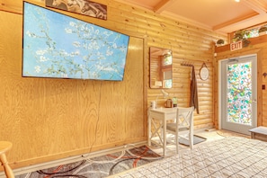 Un intérieur en bois agrémenté d’un grand tableau floral, d’un miroir, d’une petite table et d’une porte ornée d’un vitrail.
