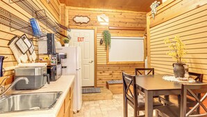 A wooden interior with a kitchen area including a sink, a coffee maker, and a refrigerator. There is a dining table with chairs and a potted plant on the table.
