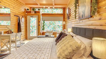 A cozy log cabin room with a bed, a desk, and a window with a stained glass view.