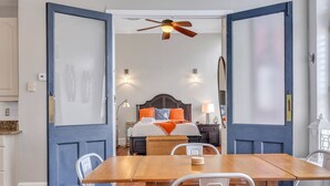 A room with a wooden dining table, white chairs, a bed with orange bedding, and a ceiling fan. - Pet Friendly, Walkable Loft in Heart of Downtown by Lucky Savannah (Savannah)