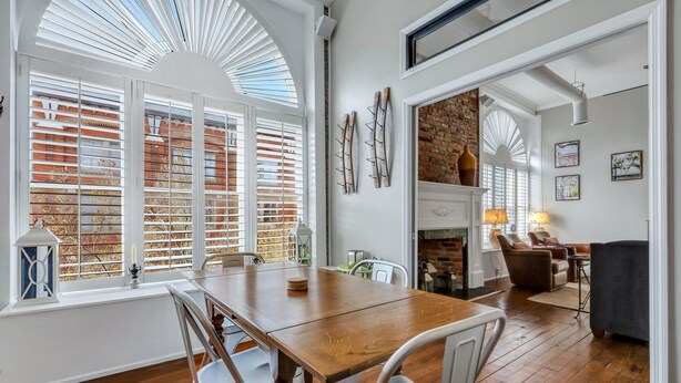 A dining area with a wooden table, white chairs, and a brick wall in the background. - Pet Friendly, Walkable Loft in Heart of Downtown by Lucky Savannah (Savannah)