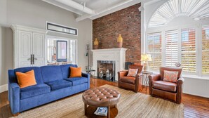 A living room with a blue sofa, brown leather ottoman, and a fireplace. - Pet Friendly, Walkable Loft in Heart of Downtown by Lucky Savannah (Savannah)