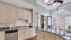 A kitchen with white cabinets, a dishwasher, a granite countertop, and a view of the outside through large windows. - Pet Friendly, Walkable Loft in Heart of Downtown by Lucky Savannah (Savannah)
