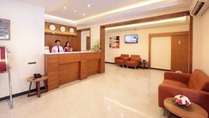 Un espace d’accueil d’hôtel comprenant un comptoir de réception en bois, un écran de télévision et un coin salon avec des canapés et des fauteuils.