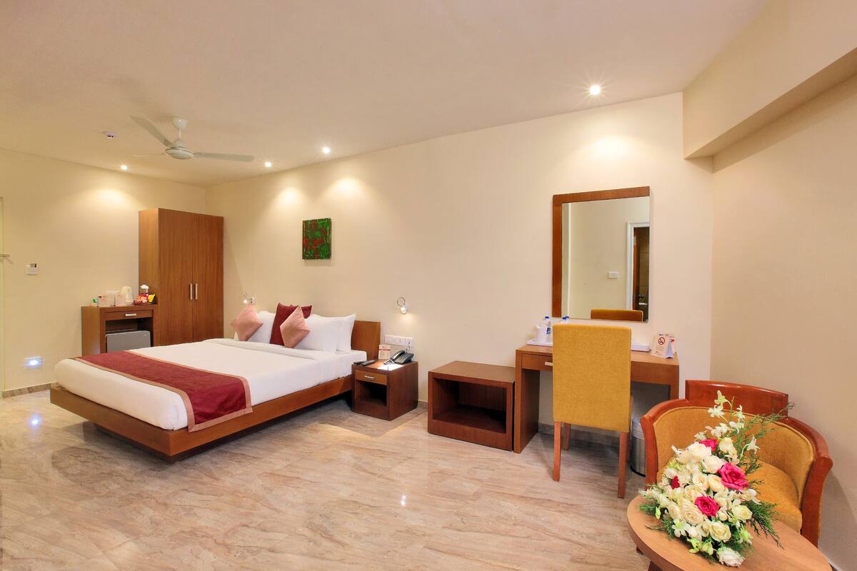 A hotel room with a bed, desk, chair, and a small table with flowers.