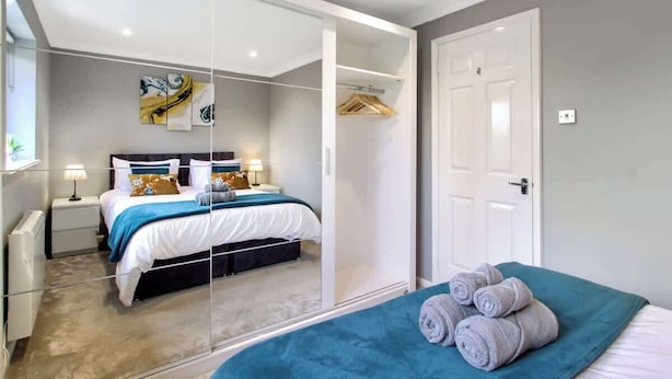 A bedroom with a bed, bedside tables, a wardrobe, and a mirror. - Spotless Two-Bedroom Home with Garden and Parking (Hertfordshire)