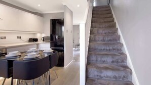 A modern kitchen with a dining area, a staircase, and a view into another room. - Spotless Two-Bedroom Home with Garden and Parking (Hertfordshire)
