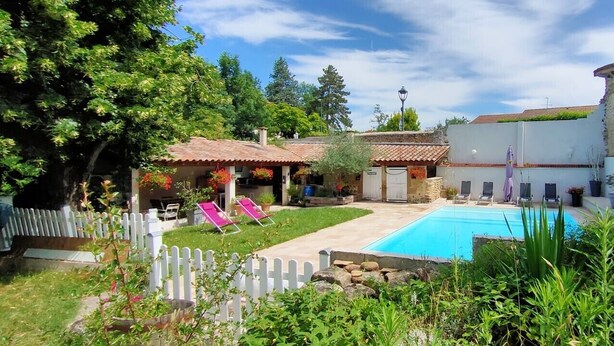 A backyard with a swimming pool, a white picket fence, and a small building with a tiled roof.