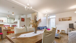 A dining area with a wooden table, chairs, a vase with dried plants, and a chandelier.