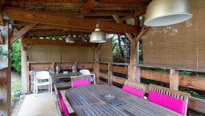 An outdoor wooden deck with a table and chairs, a hanging light fixture, and a covered seating area.