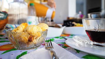 Une table mise pour le petit-déjeuner, avec un saladier en verre rempli de viennoiseries, une tasse de café et une fourchette, le tout posé sur une table recouverte d’une nappe à motifs floraux.