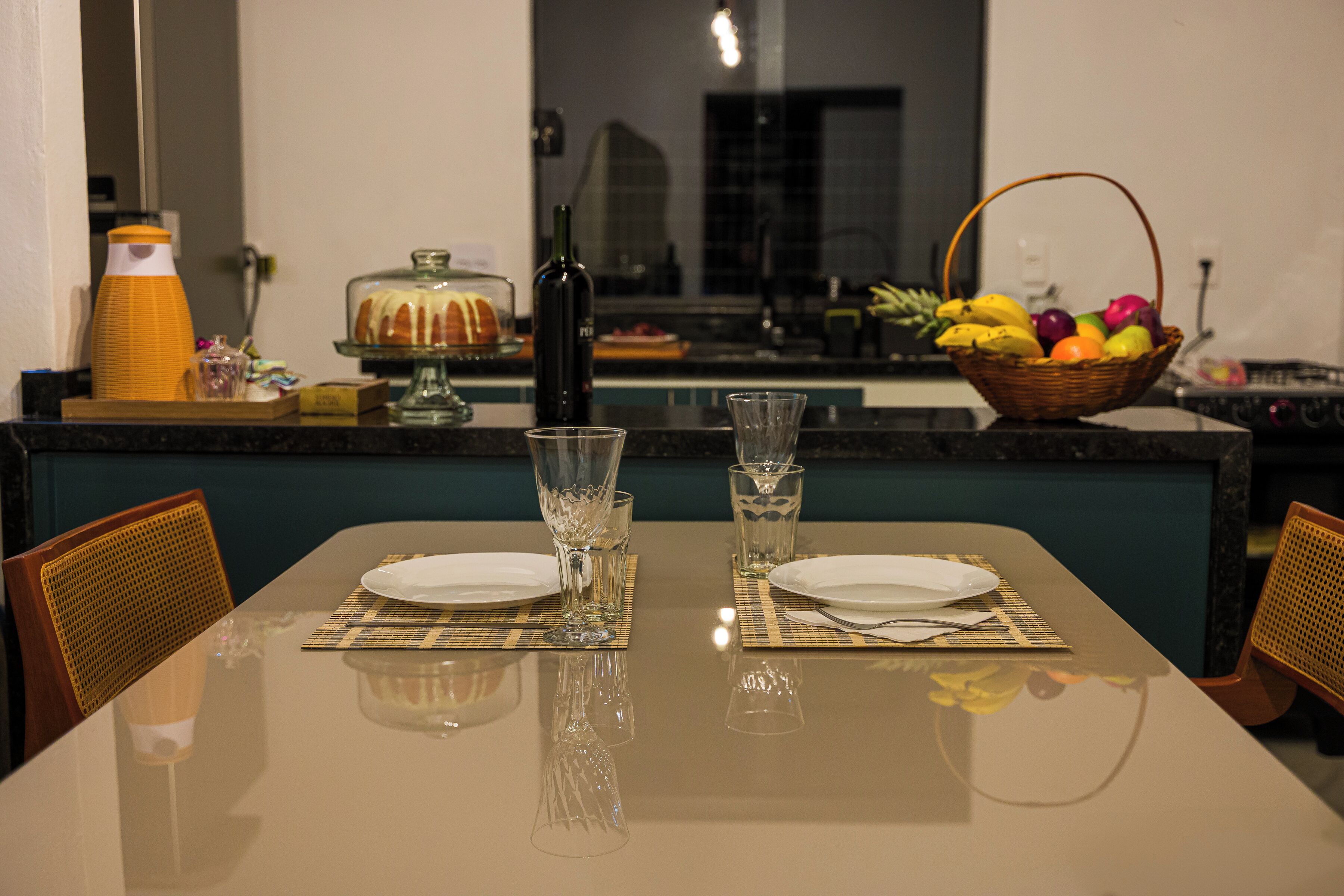 Una mesa de comedor dispuesta con platos, vasos y una cesta de frutas.