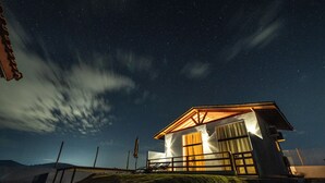 A modern house with a large window and a door, surrounded by a grassy area and a clear night sky. - Chalé Arca da Vida (Piquete)