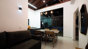 A modern living room with a dark sofa, a dining table with chairs, and a large mirror on the wall. - Chalé Arca da Vida (Piquete)