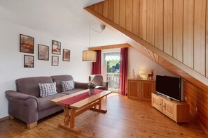 Un salon avec un canapé, une table en bois, un téléviseur et un balcon offrant une vue agréable.