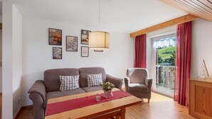 A living room with a sofa, armchair, wooden table, and a view of a green landscape through a window.