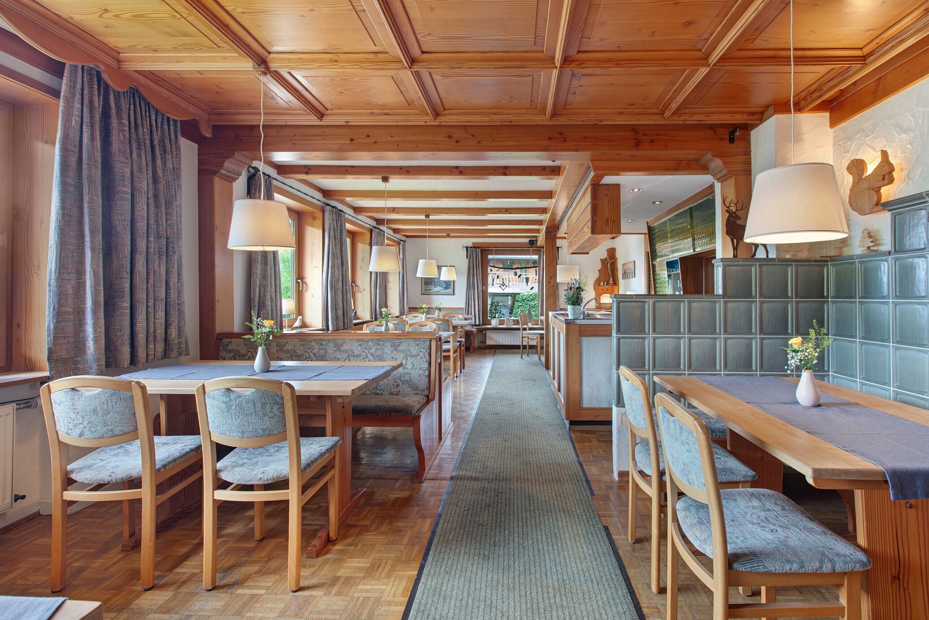 A wooden interior with a long dining table, chairs, and a kitchen area.