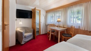 A room with a bed, a desk with a chair, a television mounted on the wall, and a window with curtains.