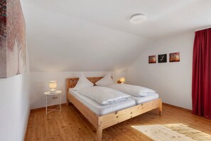 Une chambre à coucher avec un lit en bois, une literie blanche, une table de chevet avec une lampe et trois tableaux accrochés au mur.
