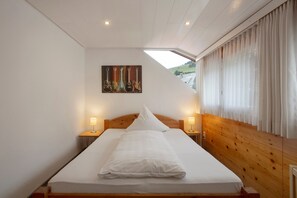A bedroom with a wooden headboard, a bed with white bedding, two bedside lamps, and a painting of guitars on the wall. - Room '16' with Mountain View, Shared Terrace and Wi-Fi (Todtnau OT Todtnauberg)