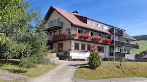 Un bâtiment à deux étages, doté d’un toit en pente, d’un balcon orné de fleurs rouges et d’une enseigne indiquant « Pension Birgl ».